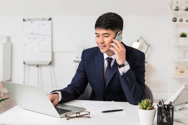 Young Asian businessman talking by phone in office