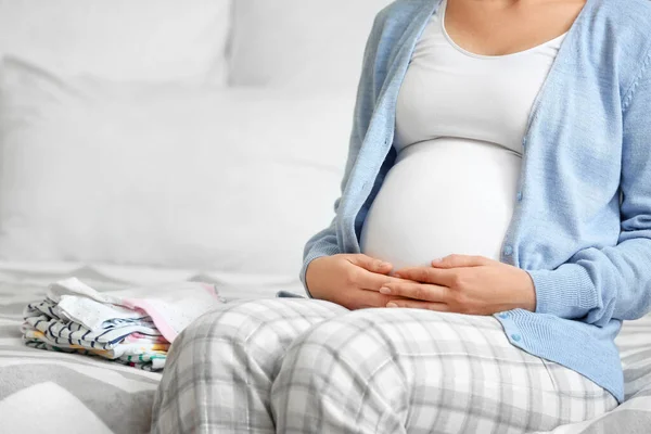 Schwangere mit Babykleidung im Schlafzimmer, Nahaufnahme — Stockfoto