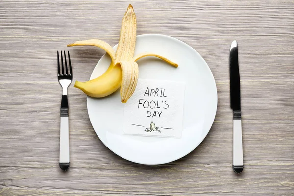 Zastawa stołowa, skórka od banana i serwetka z tekstem April Fool 's Day na drewnianym stole — Zdjęcie stockowe