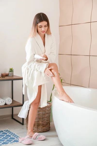 Mulher bonita aplicando creme em sua perna no banheiro — Fotografia de Stock