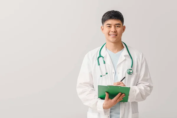 Masculino médico asiático con portapapeles sobre fondo claro — Foto de Stock