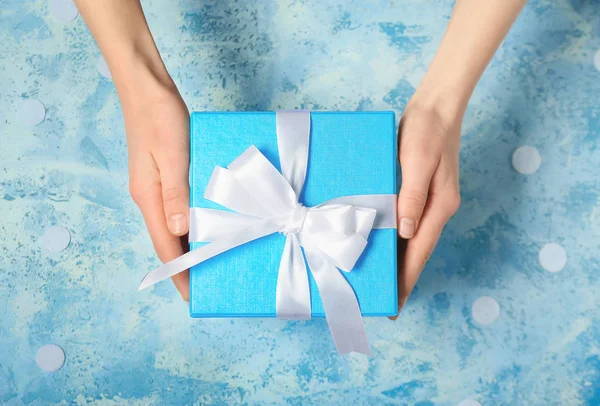 Mani femminili con bella scatola regalo su sfondo a colori — Foto Stock