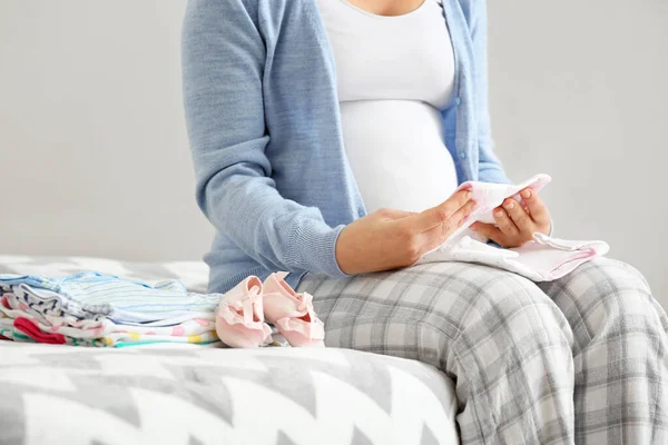 Pregnant woman with baby clothes in bedroom, closeup — Stock Photo, Image