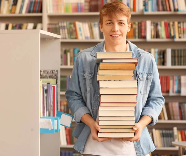 Portrét studenta s velkým stohem knih v knihovně — Stock fotografie