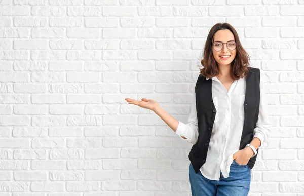 Portrait of beautiful young businesswoman showing something on white brick background — Stock Photo, Image