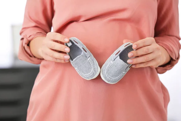Pregnant woman with baby shoes at home, closeup — Stock Photo, Image