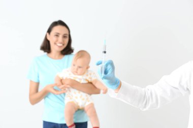 Çocuk doktoru, arka planda küçük bir bebeği aşılıyor.