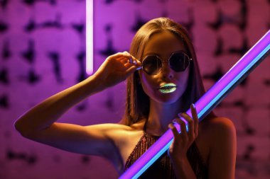 Koyu renkli arka planda neon lambalı şık bir genç kadın.
