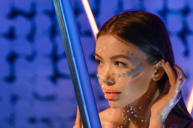 Cildinde floresan boyası olan ve arka planında neon lambası olan genç bir kadın.