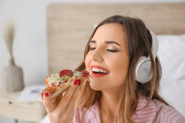 Güzel genç bir kadının lezzetli pizzalar yiyip yatak odasında müzik dinlediği bir sabah.