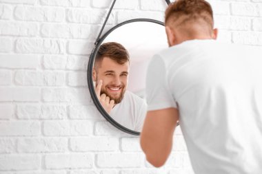 Yakışıklı genç adam banyoda aynanın yanında yüzüne krem sürüyor.