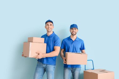 Delivery men with boxes on color background