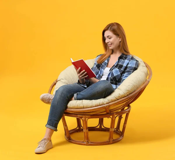 Mooie vrouw lezen boek terwijl zitten in fauteuil tegen kleur achtergrond — Stockfoto