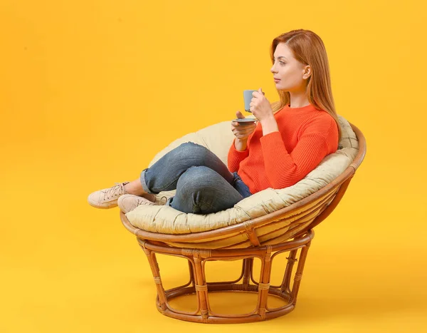 Hermosa mujer bebiendo café mientras está sentada en sillón contra el fondo de color — Foto de Stock
