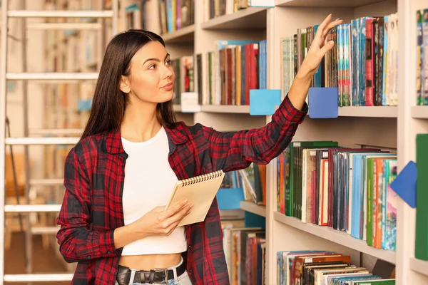 Νεαρή φοιτήτρια επιλέγει βιβλίο στη βιβλιοθήκη — Φωτογραφία Αρχείου