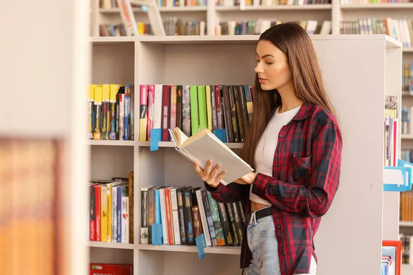Estudante do sexo feminino ler livro enquanto se prepara para o exame na biblioteca — Fotografia de Stock