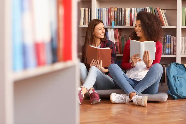 Estudantes do sexo feminino com livros se preparando para exame na biblioteca — Fotografia de Stock