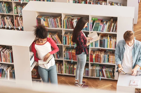 Jovens estudantes lendo livros enquanto se preparam para o exame na biblioteca — Fotografia de Stock