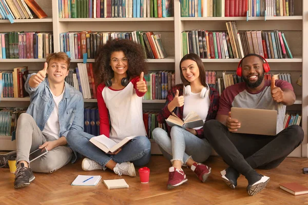 Jovens estudantes mostrando gesto de polegar para cima na biblioteca — Fotografia de Stock