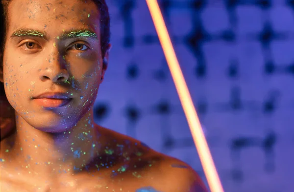 Young African-American man with fluorescent paint on his skin on color background — Stock Photo, Image