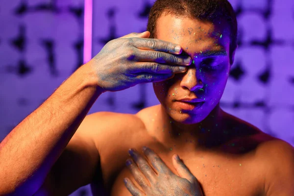 Young African-American man with fluorescent paint on his skin on color background — Stock Photo, Image