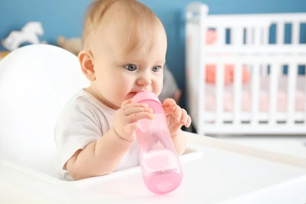 Baby with bottle of water sitting in high-chair at home — Stock Photo, Image