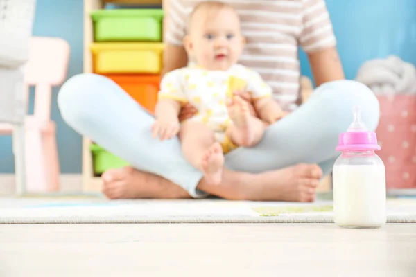 Mor med liten baby och flaska mjölk på golvet — Stockfoto
