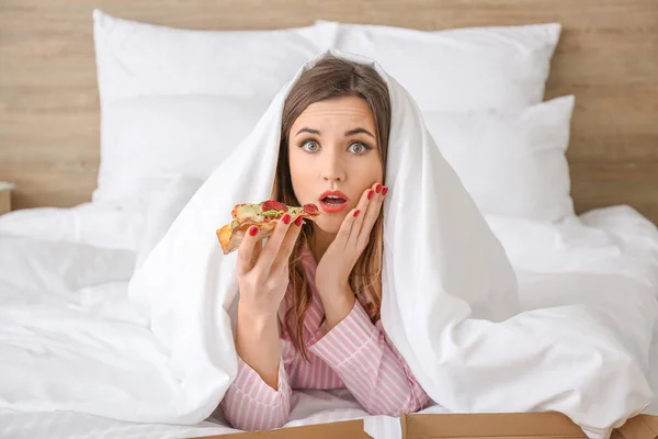 Утром красивая молодая женщина ест вкусную пиццу в спальне — стоковое фото