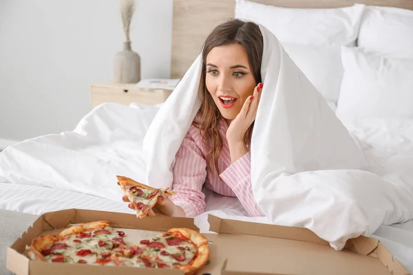 Morning of beautiful young woman eating tasty pizza in bedroom — Stock Photo, Image