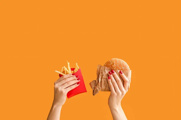 Manos femeninas con papas fritas y hamburguesa sobre fondo de color — Foto de Stock