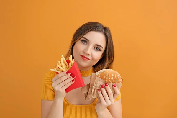 Ritratto di bella giovane donna con hamburger e patatine fritte su sfondo colore — Foto Stock