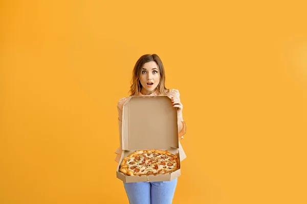Portrait of surprised young woman with tasty pizza on color background — Stock Photo, Image