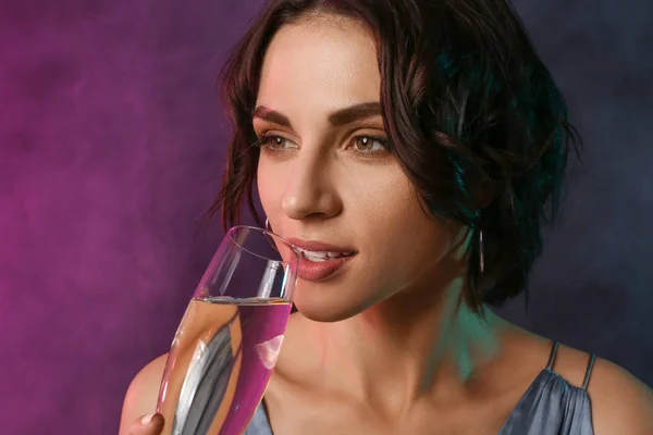 Portrait of fashionable young woman with champagne on dark color background — Stock Photo, Image