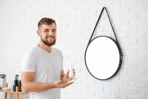 Handsome young man with tube of cream in bathroom — Stock Photo, Image