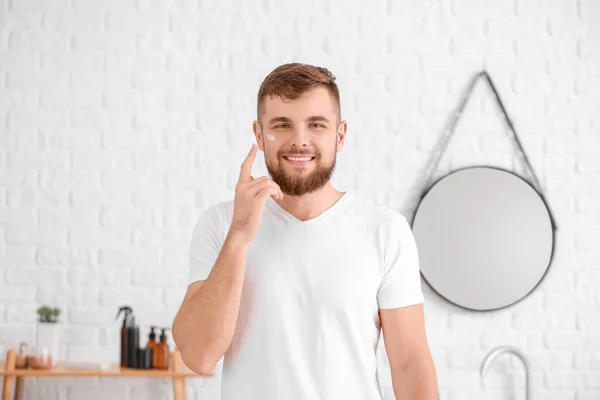 Guapo joven aplicando crema en su cara en el baño — Foto de Stock