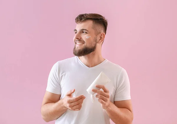 Handsome young man applying cream on his face against color background — Stock Photo, Image