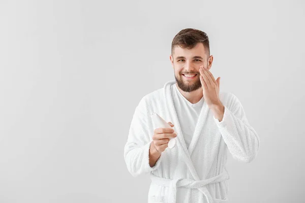Guapo joven aplicando crema en su cara sobre fondo blanco — Foto de Stock