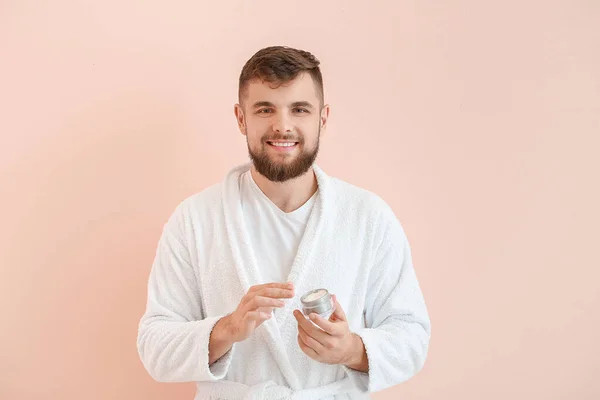 Handsome young man with jar of cream on color background — Stock Photo, Image