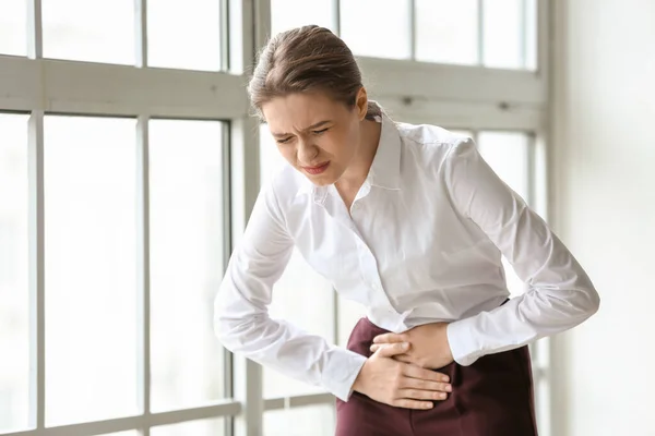 Joven empresaria que sufre de dolor abdominal en el consultorio —  Fotos de Stock