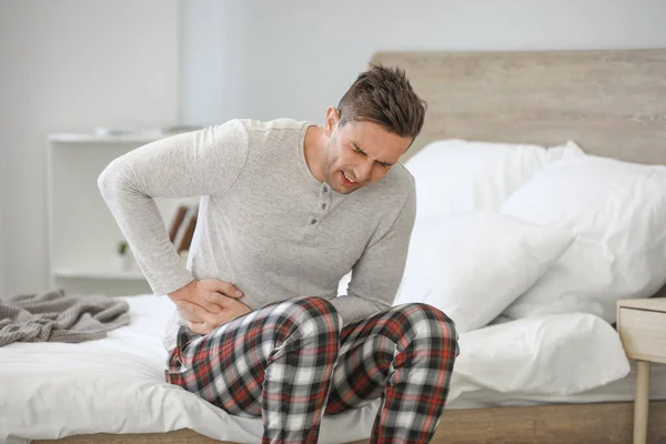 Young man suffering from abdominal pain in bedroom — Stock Photo, Image