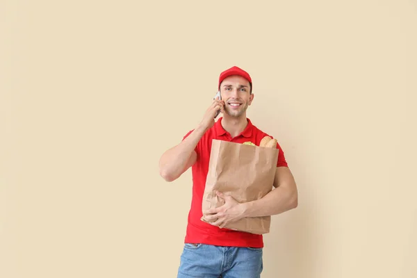 Handsome worker of food delivery service talking by phone on color background — Stock Photo, Image