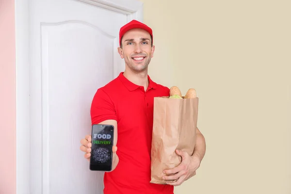 Bonito trabalhador do serviço de entrega de alimentos com telefone celular perto da porta do cliente — Fotografia de Stock