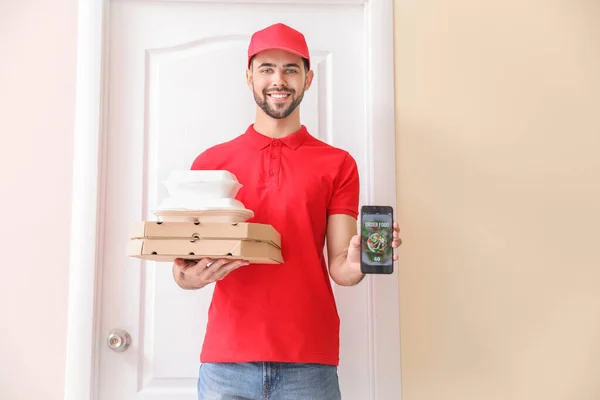 Handsome worker of food delivery service with mobile phone near customer's door — Stock Photo, Image