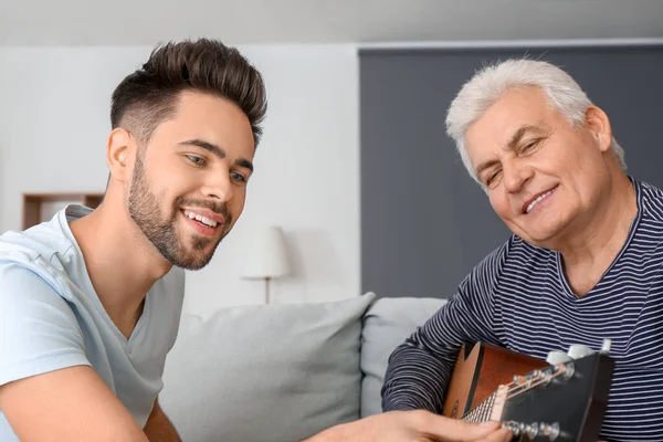 Jovem e seu pai tocando guitarra em casa — Fotografia de Stock