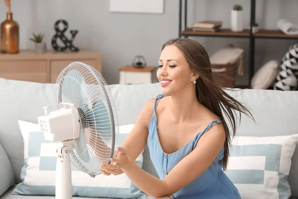 Young woman using electric fan during heatwave at home — Stock Photo, Image
