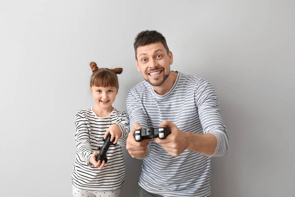 Отец и его маленькая дочь играют в видеоигры на сером фоне
