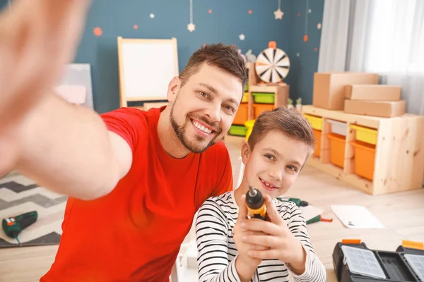 Father and his little son taking selfie while assembling furniture at home — Stock Photo, Image