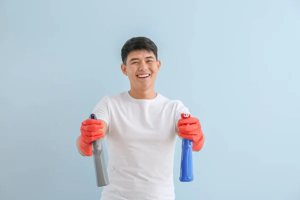 Asian man with bottles of detergents on color background — Stock Photo, Image