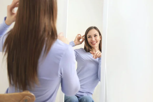 Beautiful young woman looking in mirror at home — Stock Photo, Image