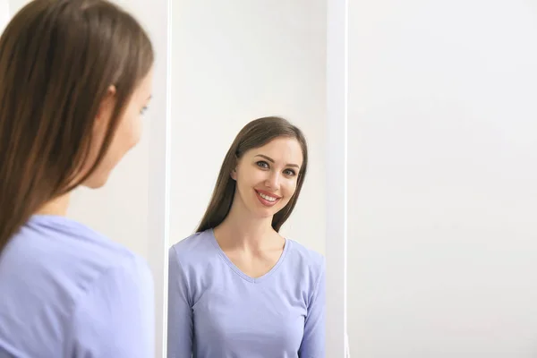 Mooie jonge vrouw kijken in spiegel thuis — Stockfoto